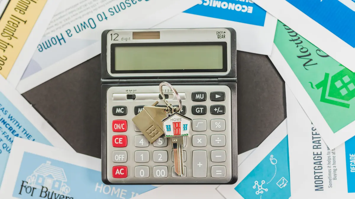 How Much Money Do You Need to Start Flipping Houses? Calculator with house keys on real estate brochures