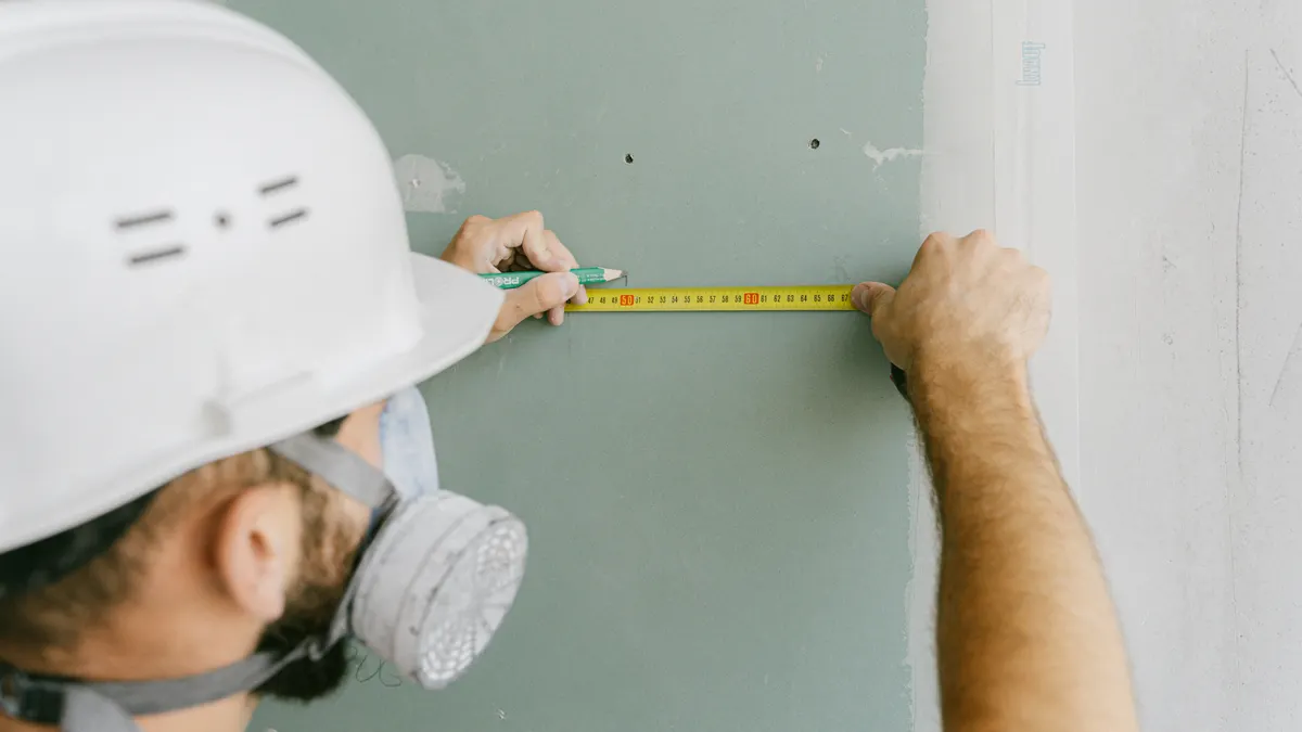 How to Estimate Repair Costs on a House Flip Worker measuring a wall with tape measure